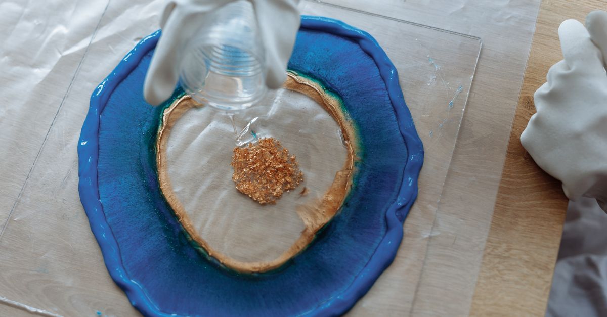 Close-up of resin art creation with blue and glitter accents being poured by gloved hands.